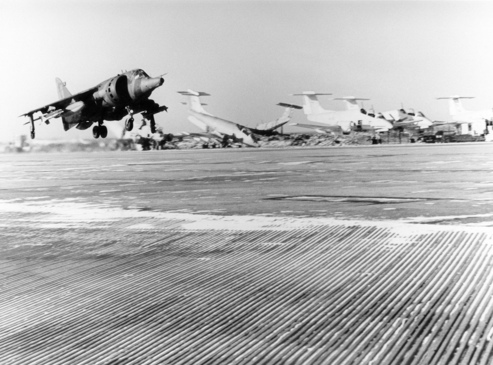 A Harrier GR3 lifting off the planked strip at Stanley airfield in 1982, aircraft and vehicles parked in the background