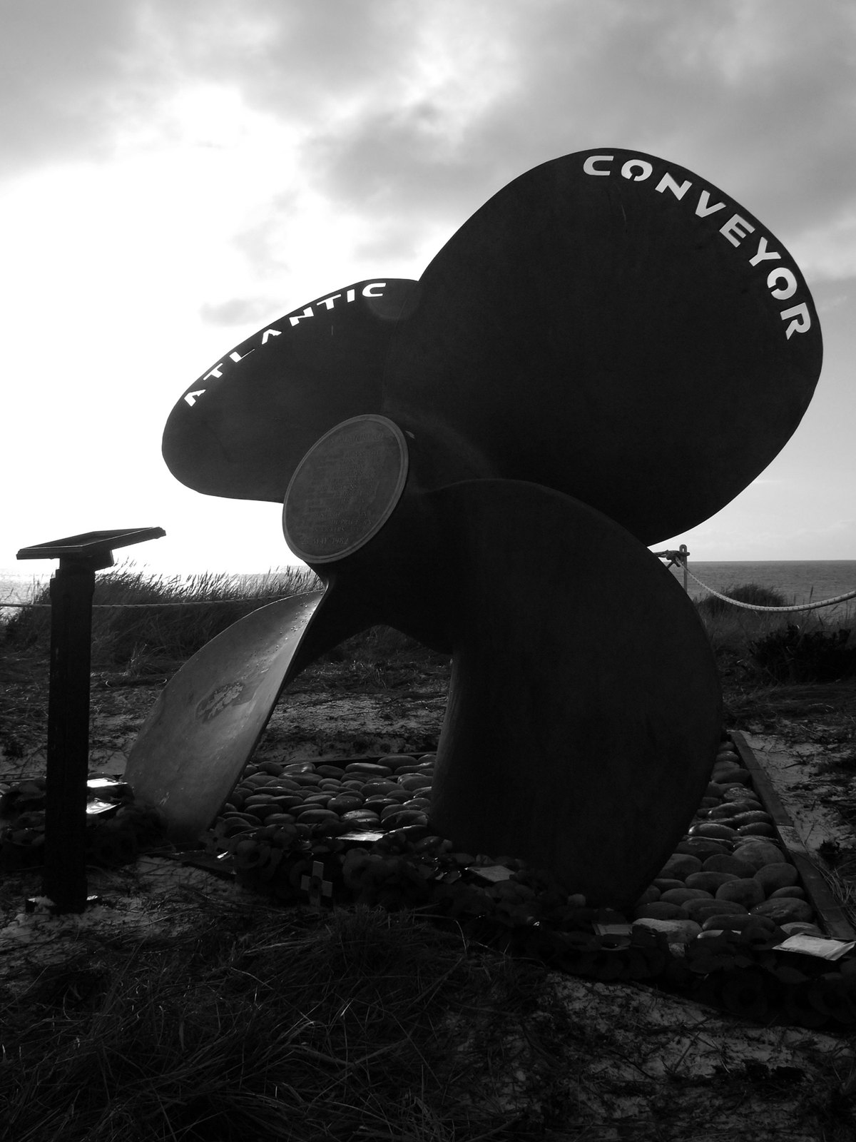 The propeller of Atlantic Conveyor set up as a memorial at Cape Pembroke, the ship's name lettered across the blades under a grey sky