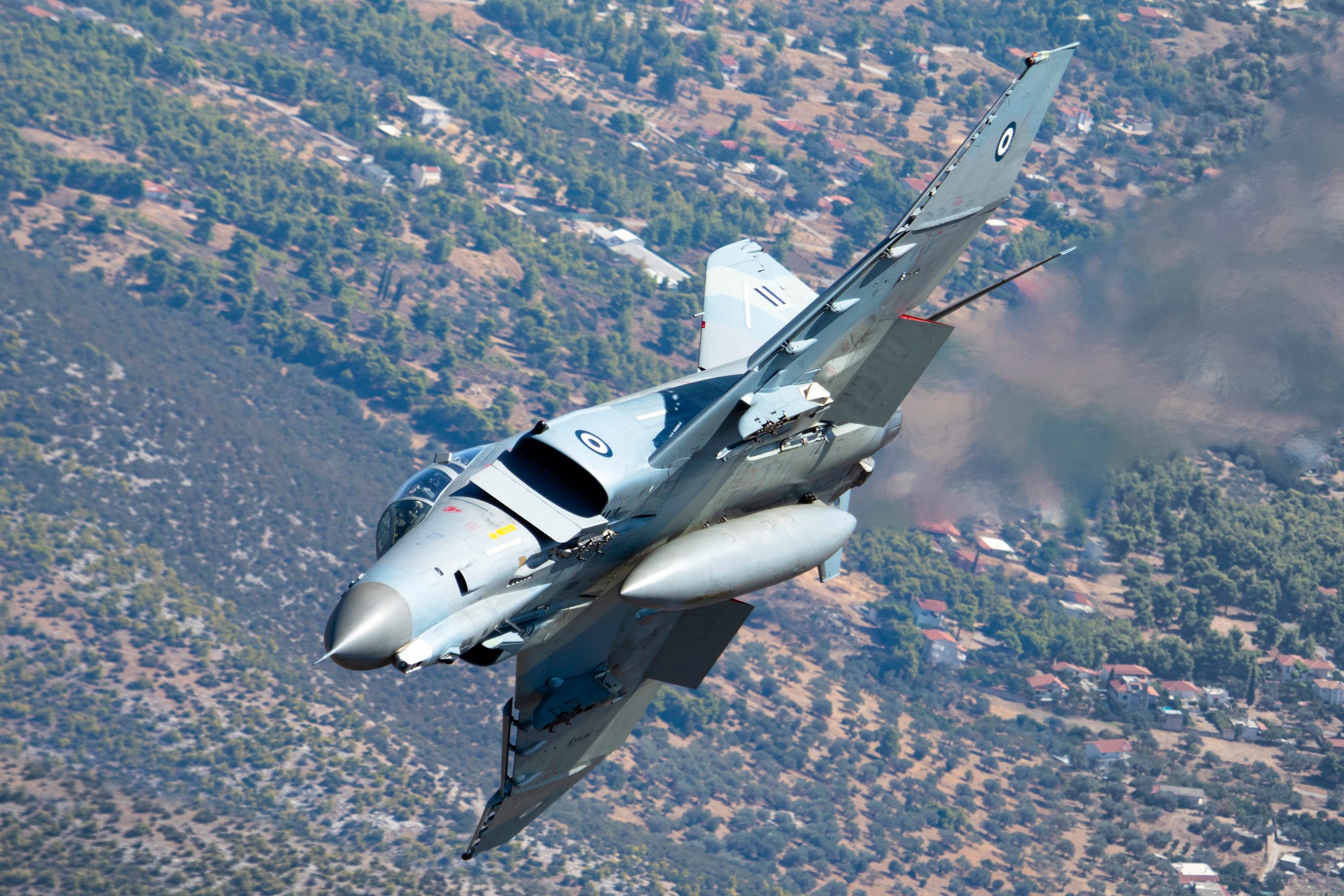 Hellenic Air Force F-4E AUP Phantom II 01518 banking hard over wooded hills, air to air
