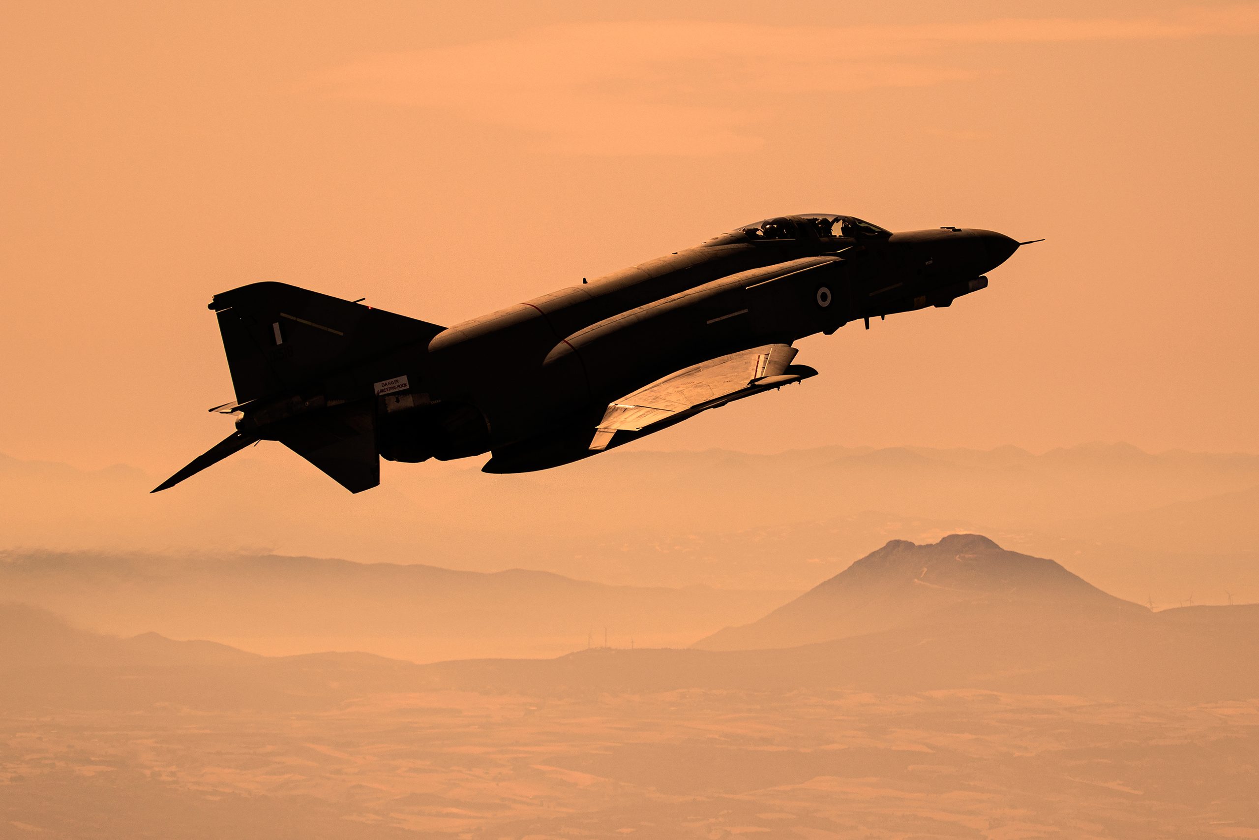 Hellenic Air Force F-4E AUP Phantom II 01518 silhouetted at dusk over hazy mountains, air to air
