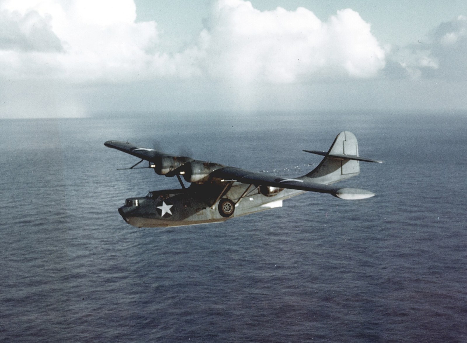 A Consolidated PBY Catalina flying boat in flight over the sea, with radar antennas beneath its wing