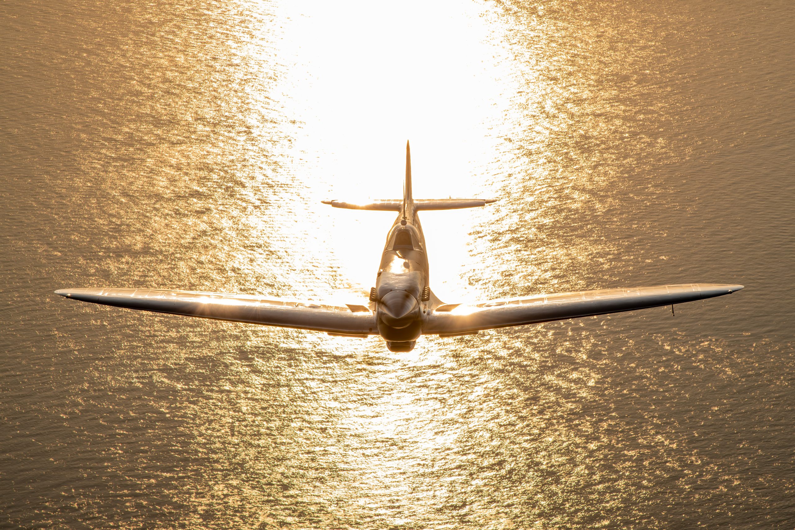 Supermarine Spitfire head-on against golden light reflecting off the sea