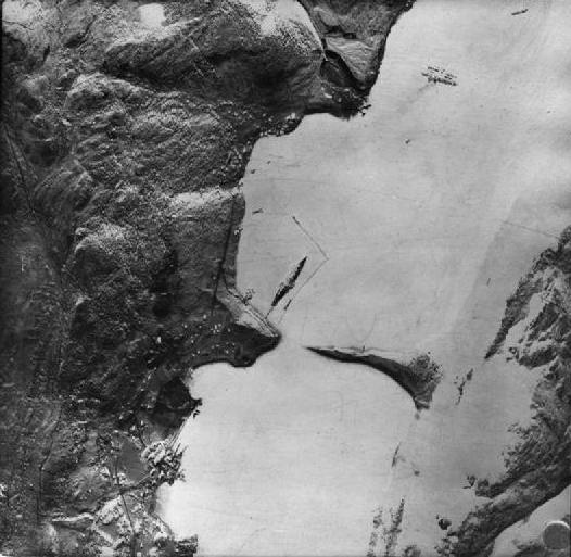 A vertical aerial reconnaissance photograph of a Norwegian fjord anchorage showing anti-torpedo net booms around a ship