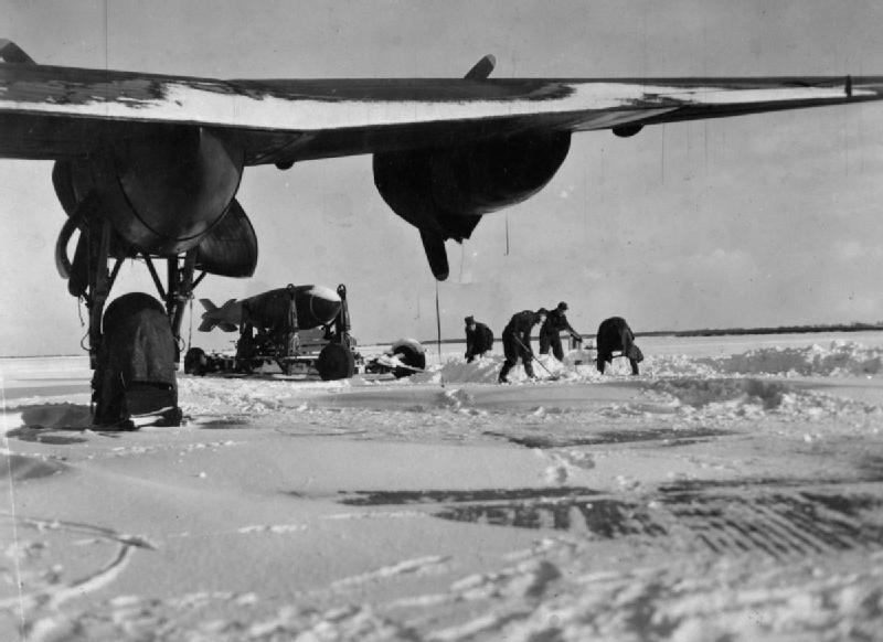 A Tallboy bomb on its wheeled trolley in deep snow beneath the wing of an Avro Lancaster