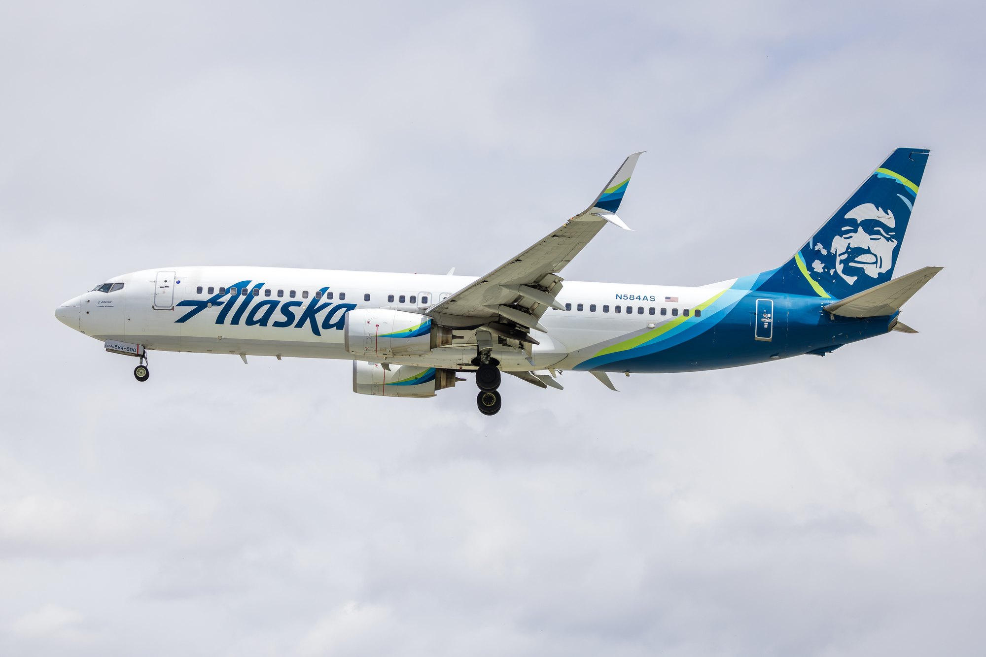 An Alaska Airlines Boeing 737-800, registration N584AS, on approach with gear and flaps extended against a pale overcast sky.