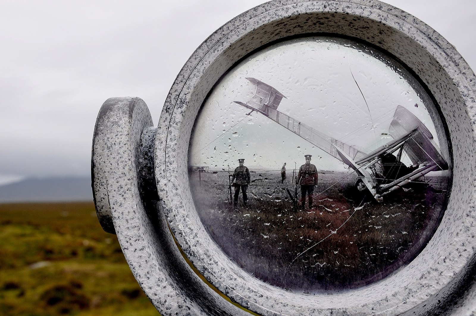 A circular viewer set in a concrete mount at Derrygimlagh, wet with rain, showing a 1919 photograph of the Vickers Vimy tipped forward on its nose in the bog with two soldiers standing guard