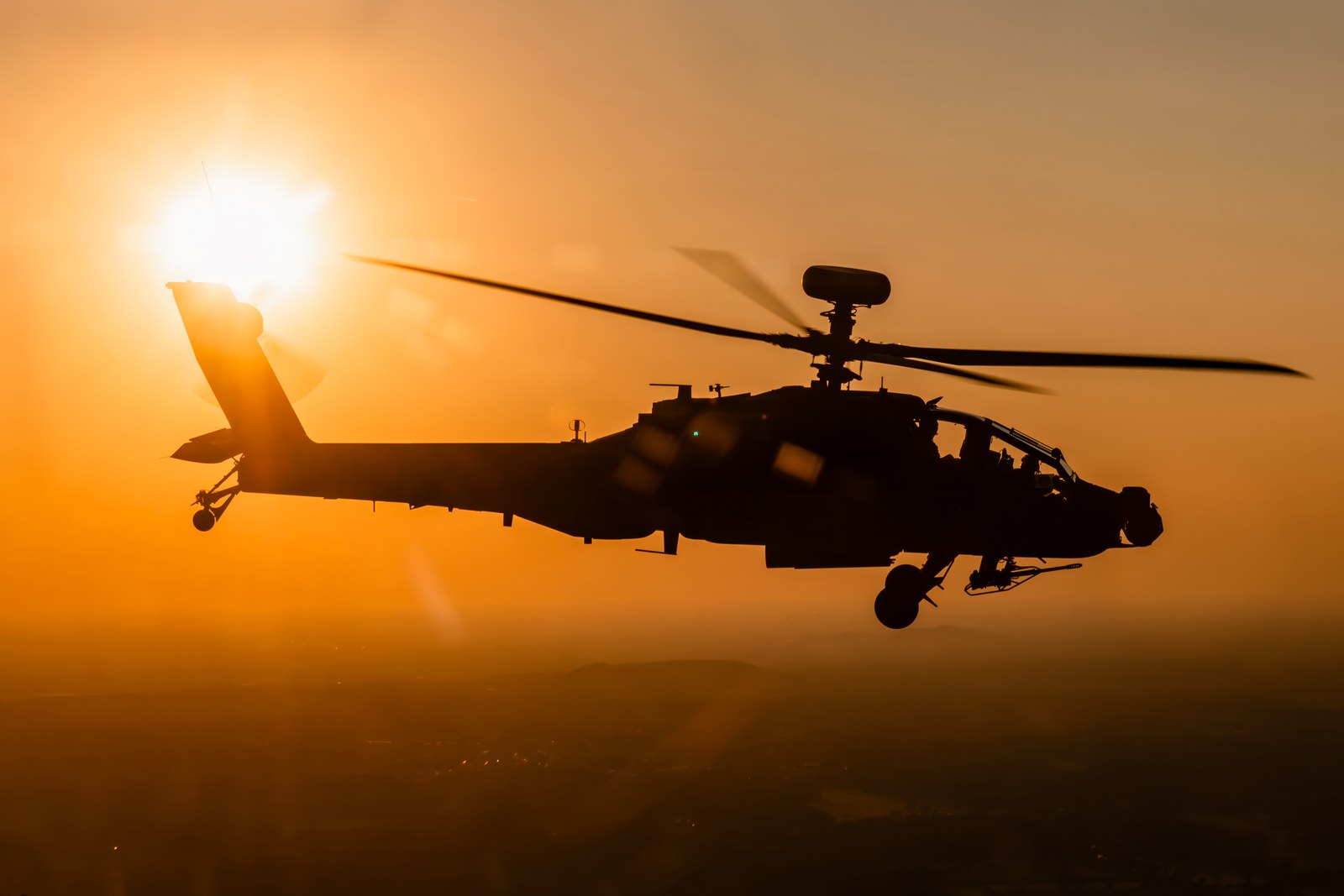 A Royal Netherlands Air Force AH-64E Apache Guardian in silhouette against the setting sun