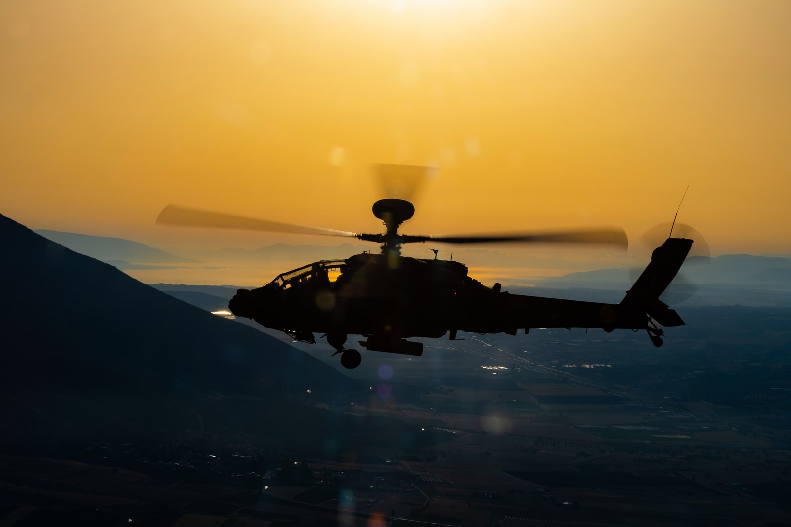 A Hellenic Army AH-64DHA Apache Longbow crossing a sky of low golden light at the end of the day