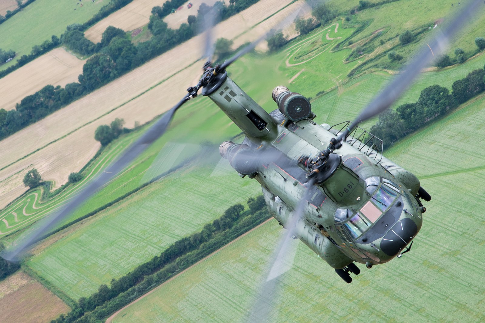 A Royal Netherlands Air Force Boeing CH-47D Chinook banking over English farmland with both rotor discs turning