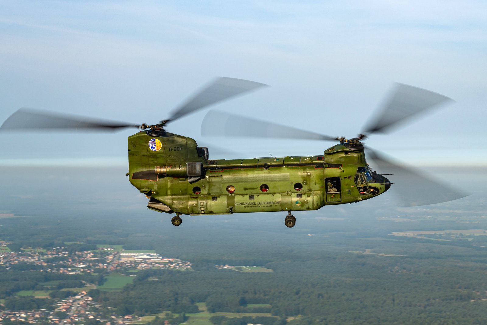 A Royal Netherlands Air Force CH-47D Chinook in side profile over Belgian countryside with the rear ramp lowered