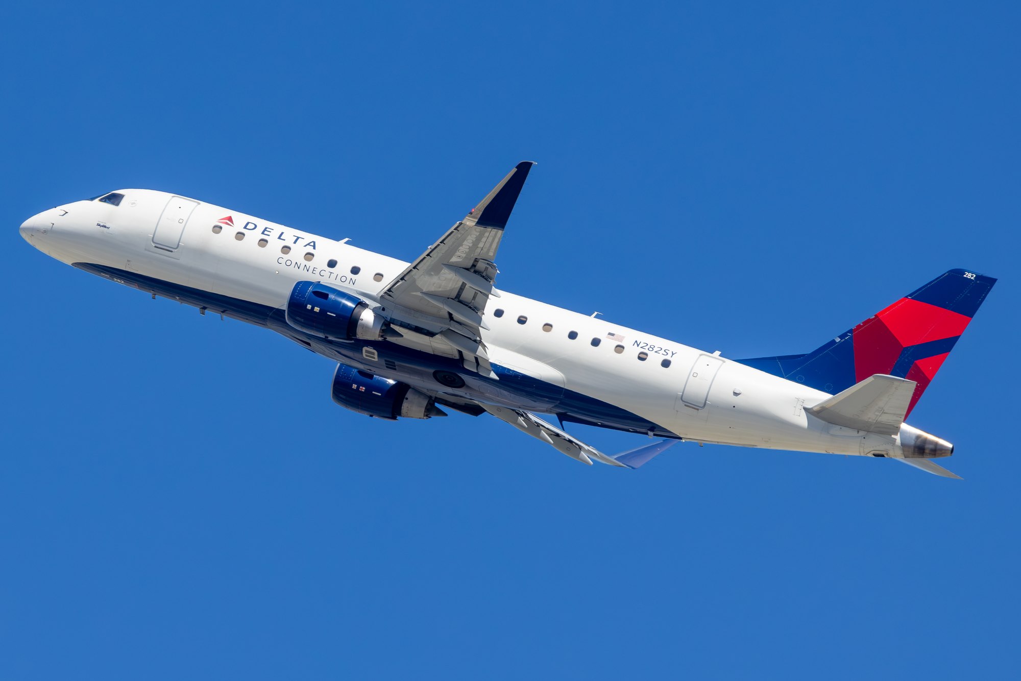A Delta Connection Embraer E175 operated by SkyWest, registration N282SY, climbing out against a deep blue sky.