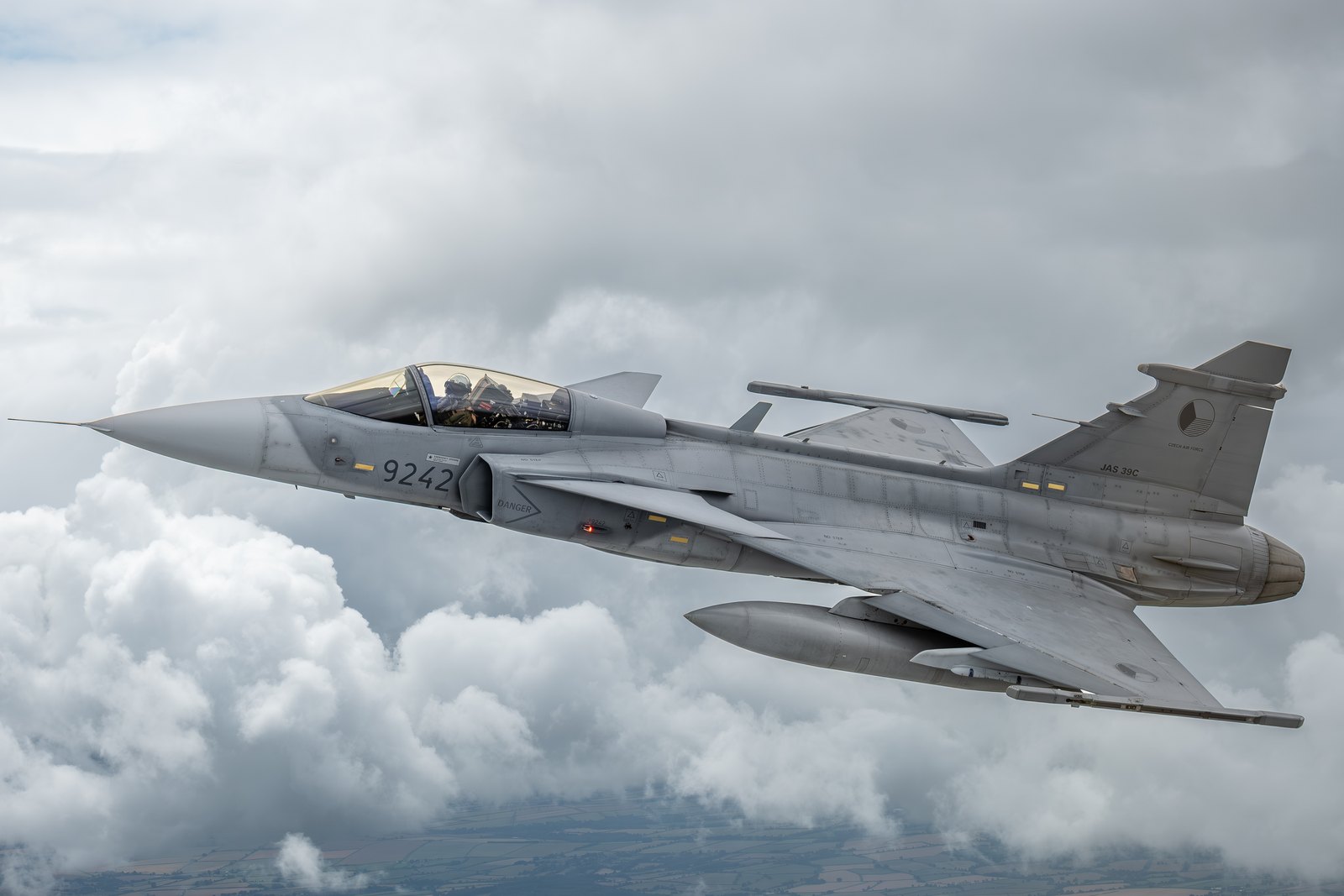 A Czech Air Force Saab JAS 39C Gripen in profile above a cloud deck with a fuel tank under the wing