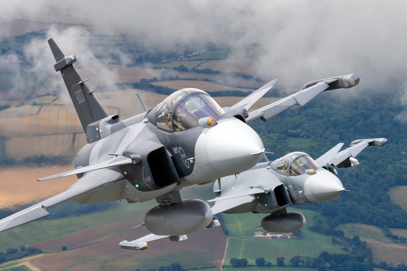 Two Saab JAS 39E Gripen fighters of the Swedish Air Force in formation over English farmland, the leader carrying the number 6003