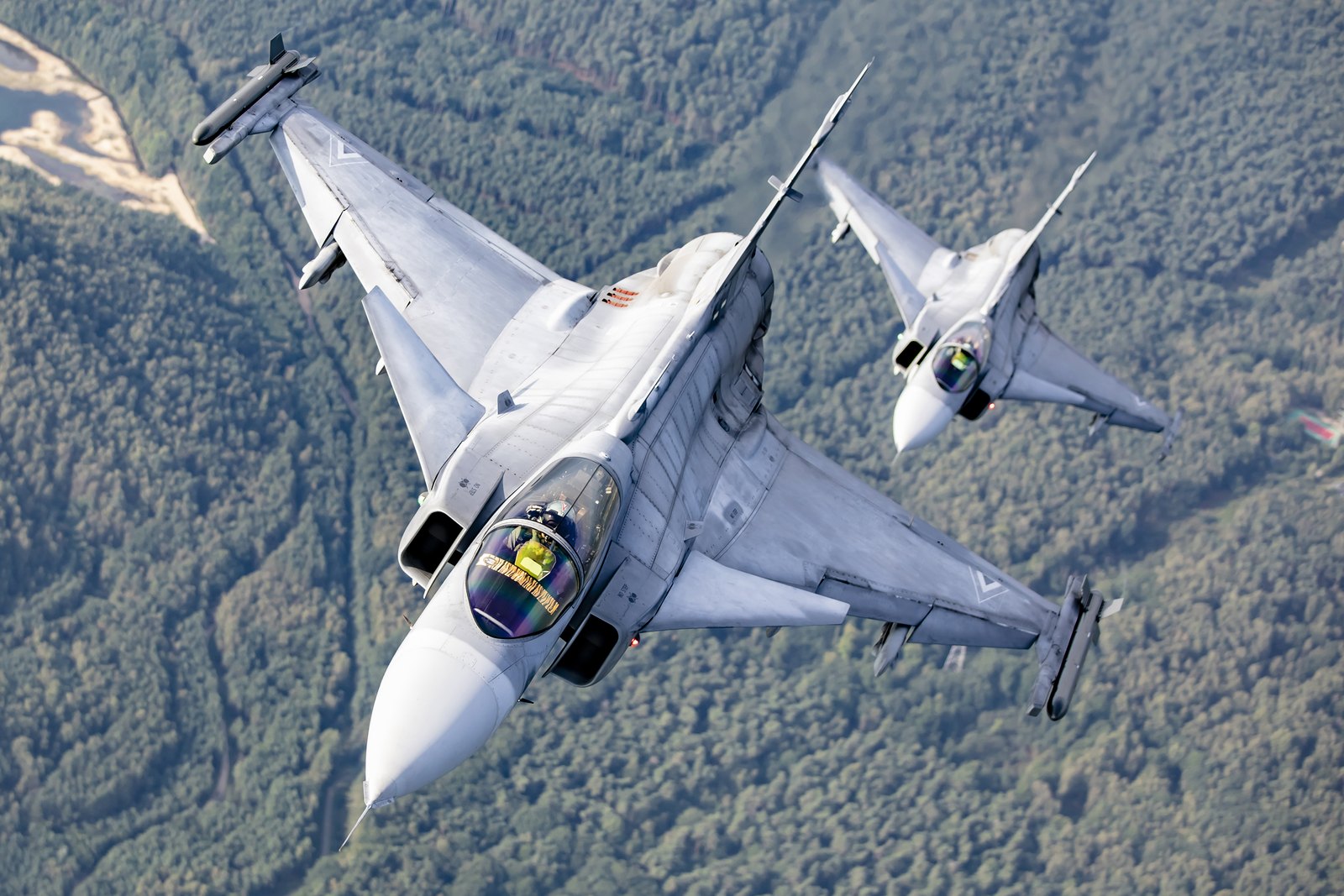 Two Hungarian Air Force Saab JAS 39C Gripens banking hard over forest, seen from above