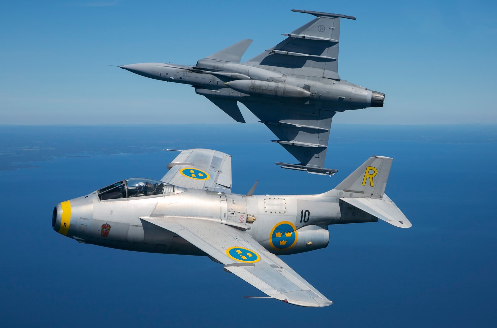 A Saab J29 Tunnan in bare metal flying in formation with an inverted Saab JAS 39C Gripen of the Swedish Air Force over the sea