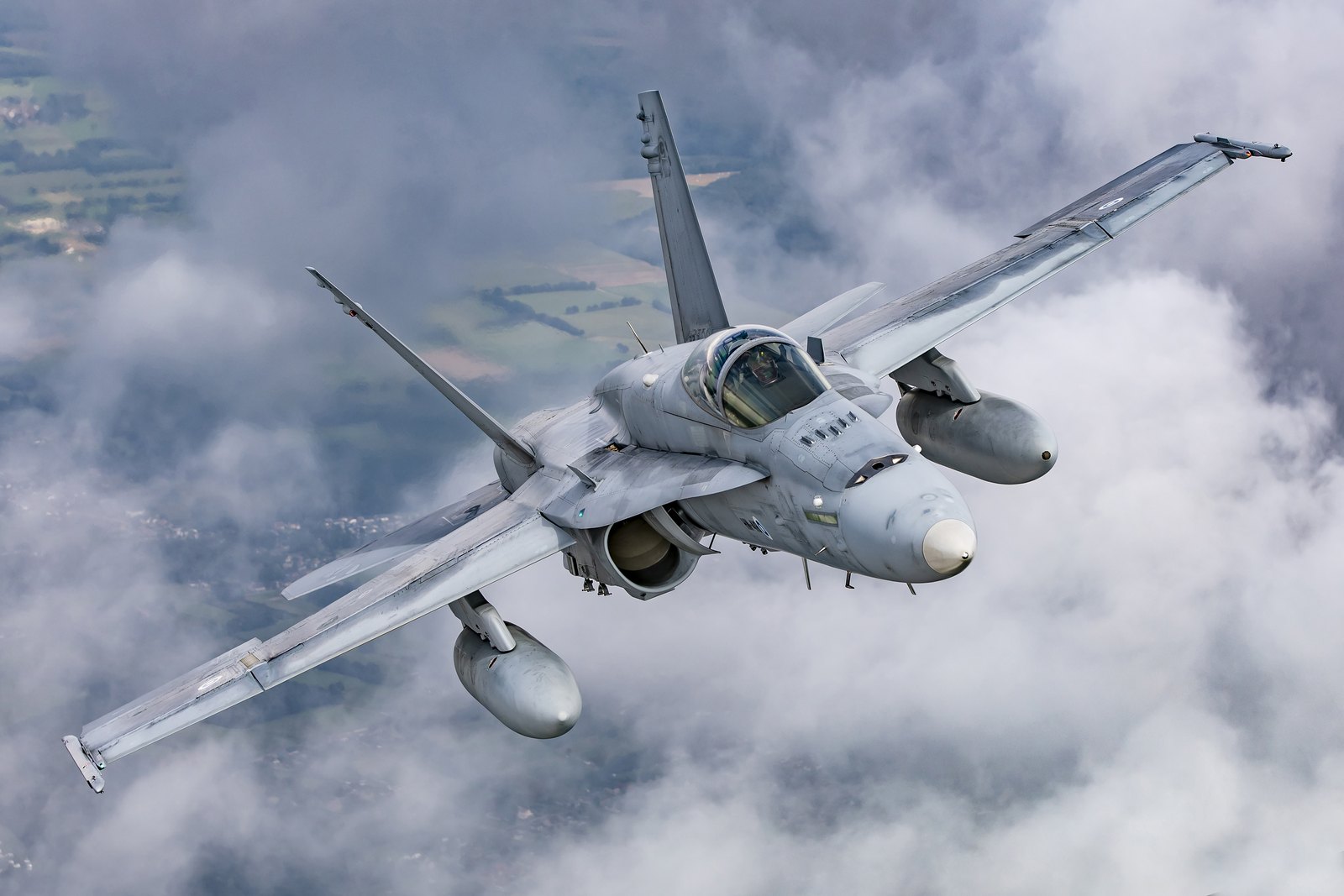 A Finnish Air Force F/A-18C Hornet turning away through cloud with a fuel tank under each wing