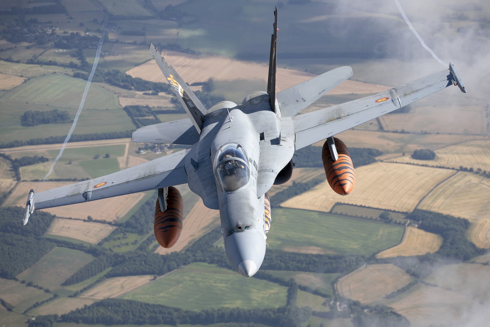 A Spanish Air Force EF-18M Hornet banking away with tiger striped fuel tanks and vortices off the wingtips