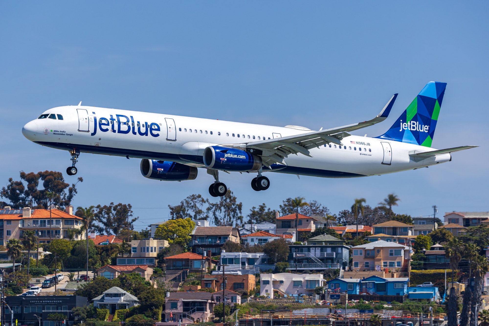 JetBlue Airbus A321 N986JB on final approach to San Diego with houses and palms below