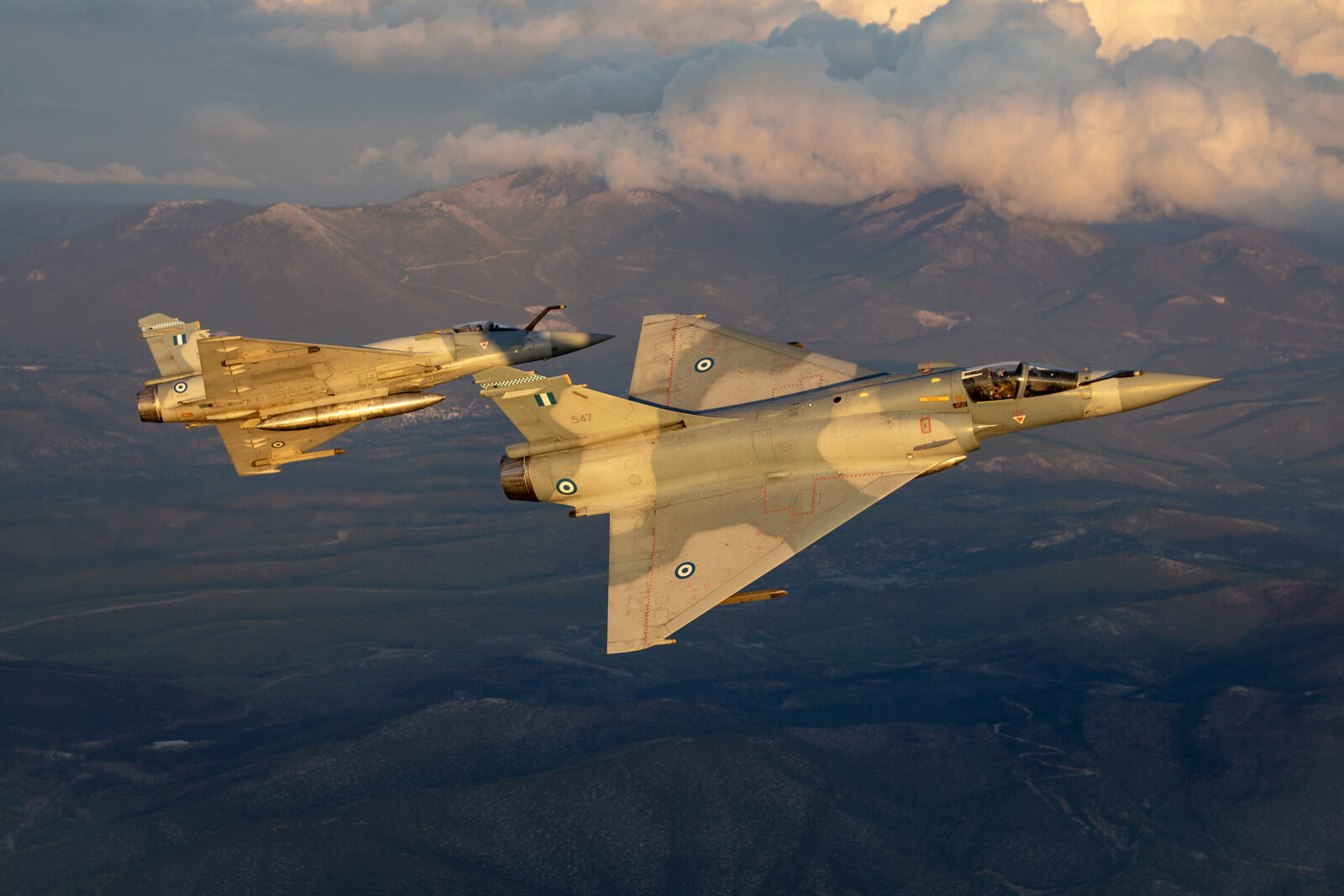 Two Hellenic Air Force Dassault Mirage 2000-5EG fighters banking in formation in evening light over the mountains
