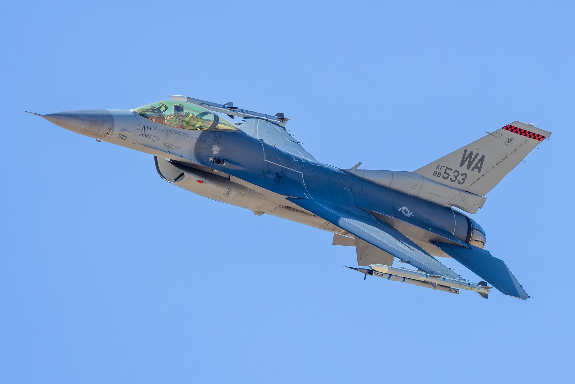 A US Air Force F-16C Fighting Falcon, tail code WA, serial 88-533, climbing away with gear retracted against a clear blue sky, the pilot visible in the canopy.